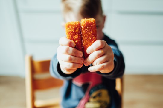 Kind hält Fischstäbchen in die Kamera