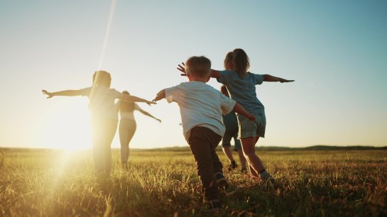 Kinder rennen auf einer Wiese mit Sonnenuntergang