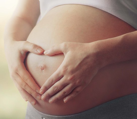 Schwangere Frau die ein Herz um ihren Bauchnabel formt