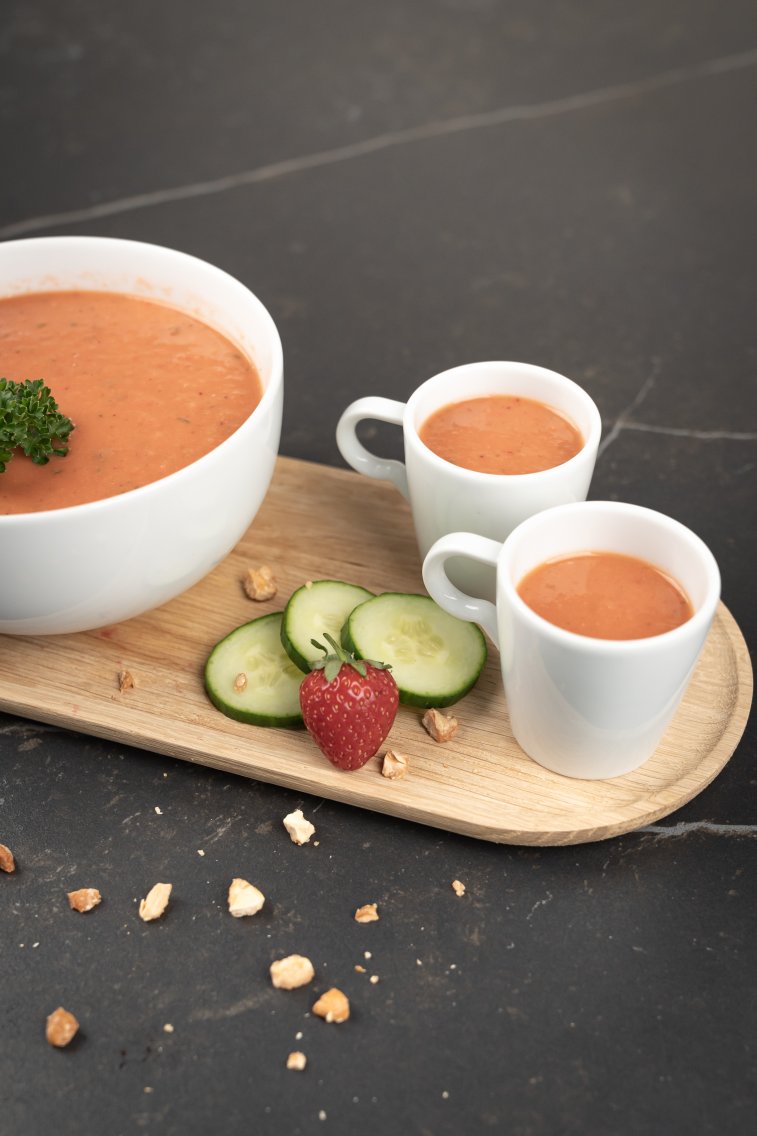 Schale mit Gazpacho, garniert mit Petersilie, Chilischote, Gurkenscheiben und Erdbeeren.