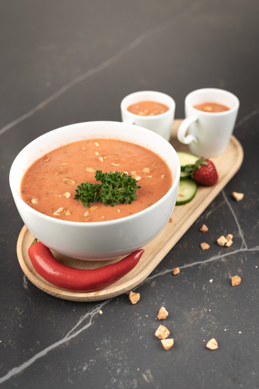 Schale mit Gazpacho, garniert mit Petersilie, Chilischote, Gurkenscheiben und Erdbeeren.