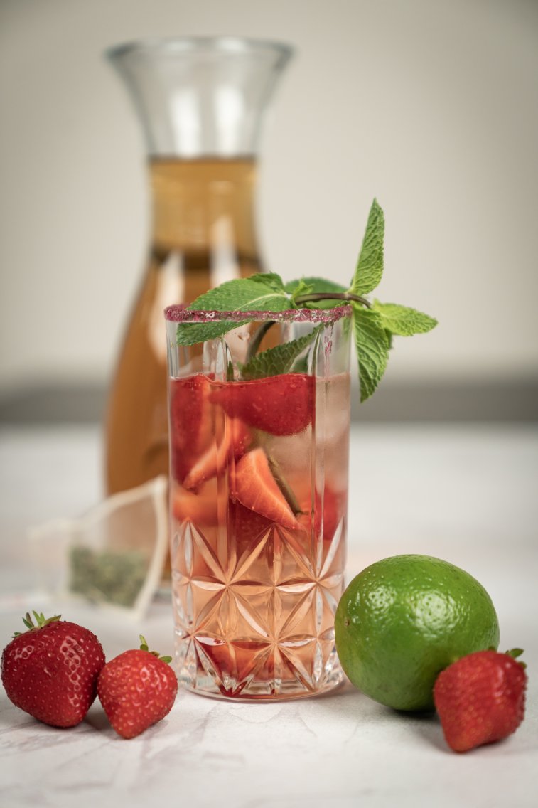 Glas mit dem Drink, garniert mit frischer Minze, Erdbeeren und einer Limette.