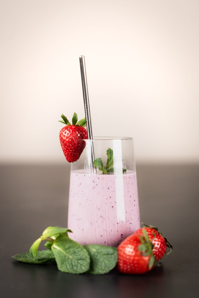 Ein Glas mit leckerem Beeren-Protein-Shake und einem Strohalm aus Metall und einer Erdbeere am Glasrand aufgesteckt