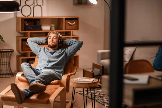 A young man is relaxing in the living room, listening to music with headphones on